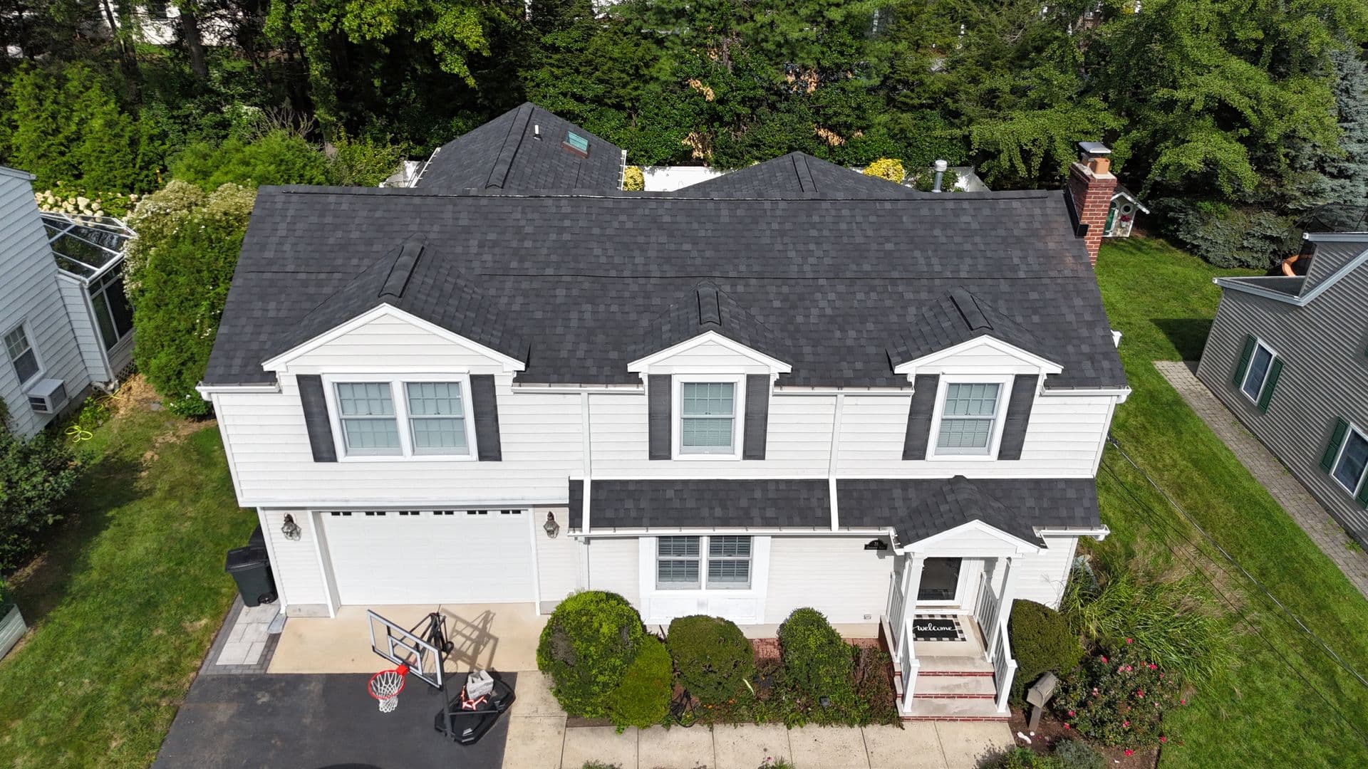 Aerial view of a white two-story home with Black Shadow architectural shingles and three front-facing dormers.